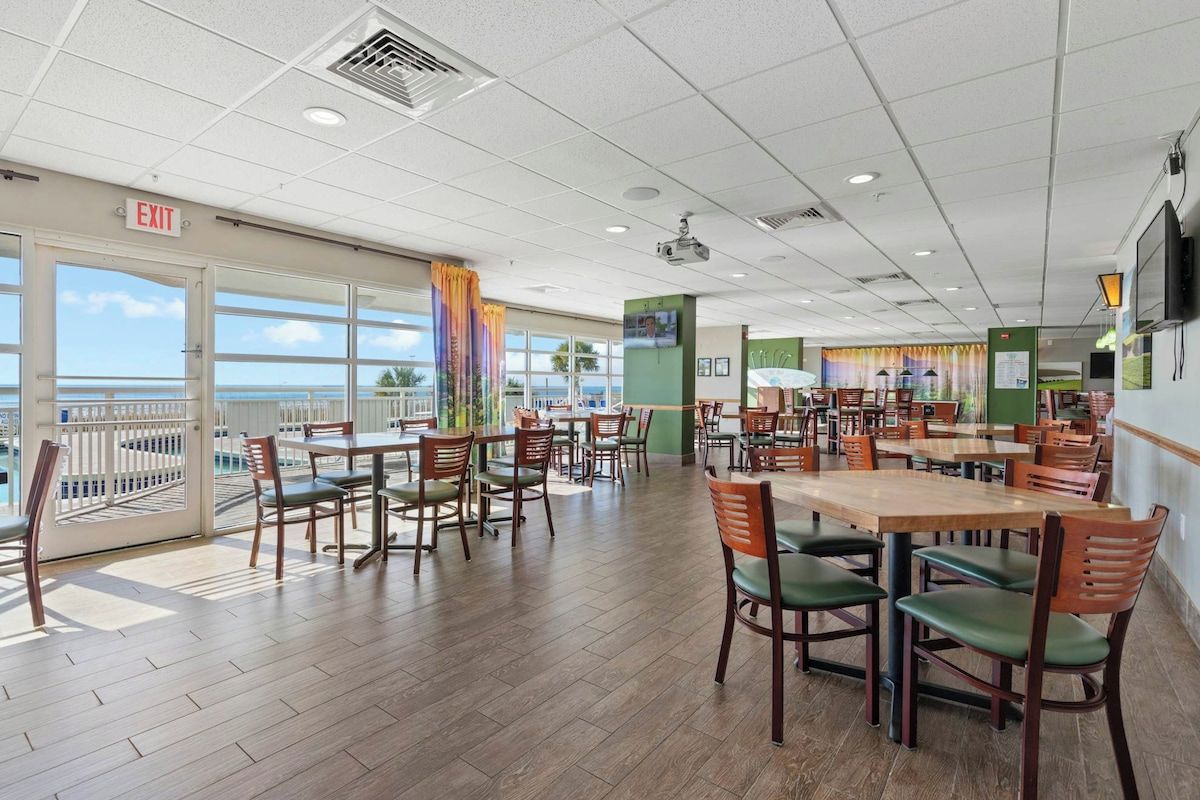 Un restaurant avec plusieurs tables et chaises, un panneau indiquant la sortie et une vue sur l’océan.