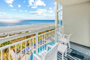 Varanda com vista para a praia e o oceano, cadeiras brancas e área de piscina.
