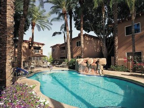Ein Pool mit Felsen, umgeben von Palmen und Liegestühlen.