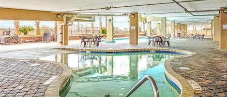 An indoor swimming pool with a tiled deck, surrounded by lounge chairs and tables.