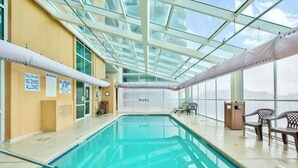 Una piscina interior amb sostres de vidre transparent, senyals de seguretat i vista del cel.