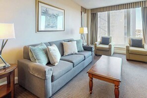 Ein Hotelzimmer mit grauem Sofa, zwei Sesseln, einem Holztisch und einem gerahmten Bild an der Wand.
