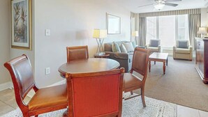 Et hotelværelse med spisebord, stole, sofa, fjernsyn og ventilator.