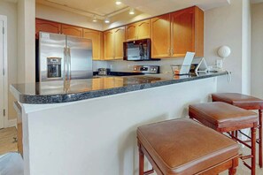 A kitchen with a stainless steel refrigerator, a microwave, and a coffee maker on the countertop. There are wooden cabinets and a granite countertop. - Bahama Sands Unit 0910 (North Myrtle Beach)