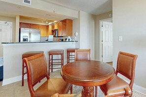 A kitchen with wooden cabinets, a stainless steel refrigerator, and a dining area with a round wooden table and four chairs. - Bahama Sands Unit 0910 (North Myrtle Beach)