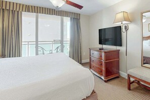 Ein Hotelzimmer mit einem großen Bett, einem Schminktisch, einem Fernseher und einem Balkon mit Vorhängen.
