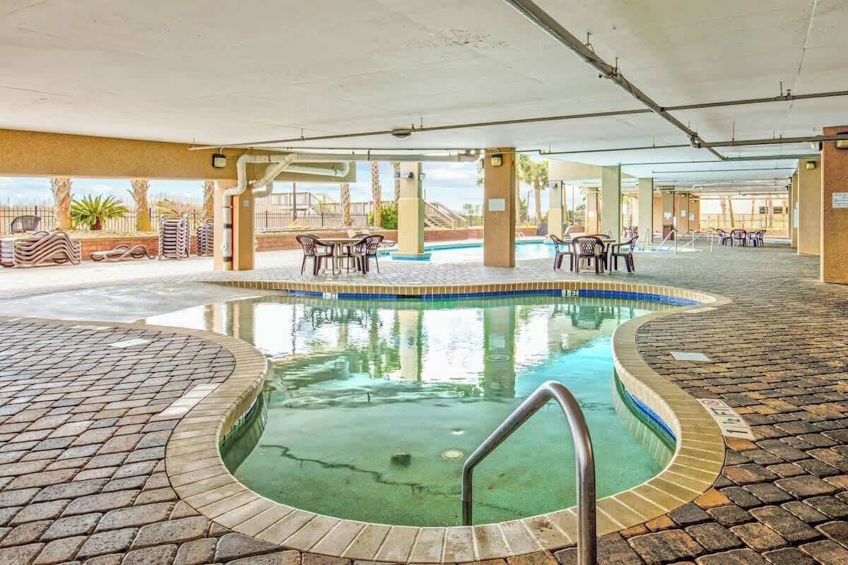 Een binnenzwembad met betegeld zonnedek, omringd door ligbedden en tafels.