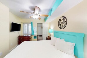 Una habitación de hotel con una cama, un ventilador de techo, un televisor y una puerta que da a un baño.