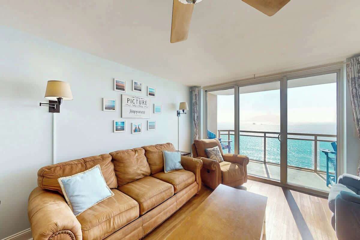 Ein Zimmer mit braunem Ledersofa, einem Holztisch und Meerblick durch große Fenster.