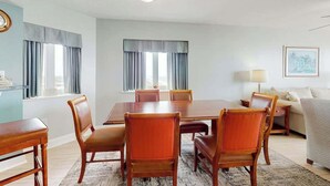 A hotel room with a dining table, six chairs, a sofa, a lamp, and a framed picture on the wall. - Bahama Sands Unit 1002 (North Myrtle Beach)