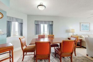 Quarto de hotel com uma mesa de jantar, seis cadeiras, um sofá, uma luminária e um quadro na parede.