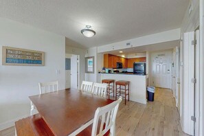 Un coin repas avec une table en bois et des chaises blanches, une cuisine avec des meubles en bois et une porte blanche.