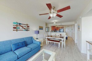 Ein Wohnzimmer mit einem blauen Sofa, einem Couchtisch, einem Deckenventilator und einem Essbereich mit einem weißen Tisch und Stühlen.