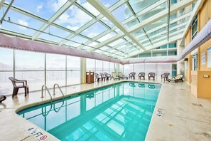Una gran piscina interior amb sostres de vidre transparent, gandules i vistes a la ciutat.