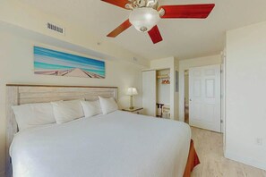 Une chambre d’hôtel avec un grand lit, un ventilateur de plafond, un tableau au mur et une porte donnant sur une autre pièce.