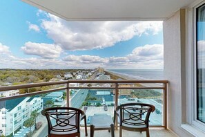 Ein Balkon mit zwei Stühlen und einem Tisch, der auf eine Küstenstadt mit Gebäuden und einem Strand blickt.
