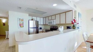 A modern kitchen with a central island, stainless steel appliances, and a dining area with a wooden table and chairs. - Bay Watch Resort 0202 (North Myrtle Beach)