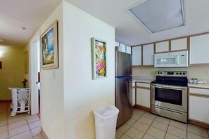 A kitchen with stainless steel appliances, white cabinets, and a trash bin. - Bay Watch Resort 0202 (North Myrtle Beach)