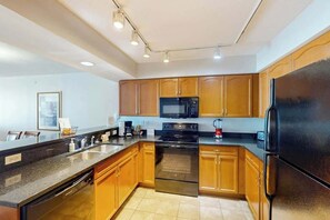 A modern kitchen with wooden cabinets, stainless steel appliances, and a granite countertop. - Bahama Sands Unit 1003 (North Myrtle Beach)