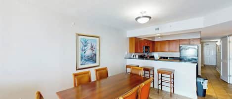 A dining area with a wooden table and chairs, a kitchen with wooden cabinets, and a small island with a refrigerator and microwave.