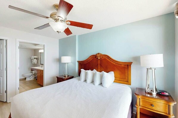 Une chambre d’hôtel avec un lit, un ventilateur de plafond, une table de chevet avec une lampe et une tête de lit en bois.
