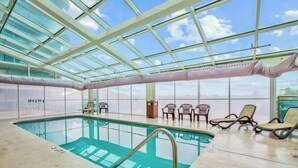 En inomhuspool med ett tak av genomskinligt glas, solstolar och utsikt mot himlen.