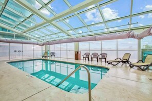 Ein Innenpool mit Glasdecke, Liegestühlen und Blick zum Himmel.