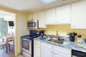 A compact kitchen with white cabinets, a stove, microwave, and a sink with a marble countertop. - Bay Watch Resort 0203 (North Myrtle Beach)