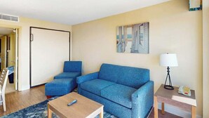 Une pièce avec un canapé bleu, une table basse en bois, une lampe et un tableau accroché au mur.