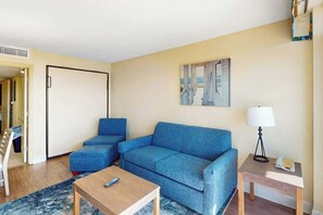 Ein Zimmer mit einem blauen Sofa, einem Holztisch, einer Lampe und einem Bild an der Wand.