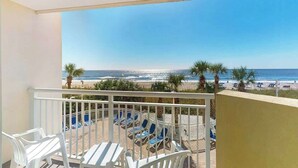 Un balcon avec vue sur la plage, des chaises blanches et une table.