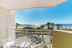 Ein Balkon mit Blick auf den Strand, weißen Stühlen und einem Tisch.
