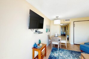 Un salon avec un téléviseur à écran plat fixé au mur, une table basse en bois, un tapis bleu et un canapé bleu.