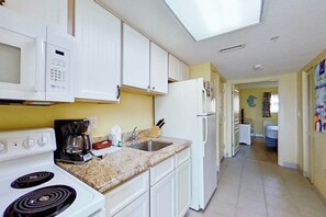A kitchen with white cabinets, a microwave, a stove, a sink, and a refrigerator. - Bay Watch Resort 0206 (North Myrtle Beach)
