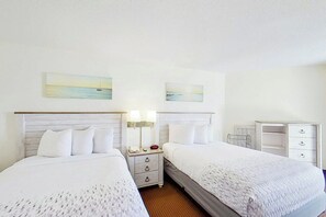 A hotel room with two beds, a nightstand with lamps, a dresser, and artwork on the walls. - Bay Watch Resort 0412 (North Myrtle Beach)