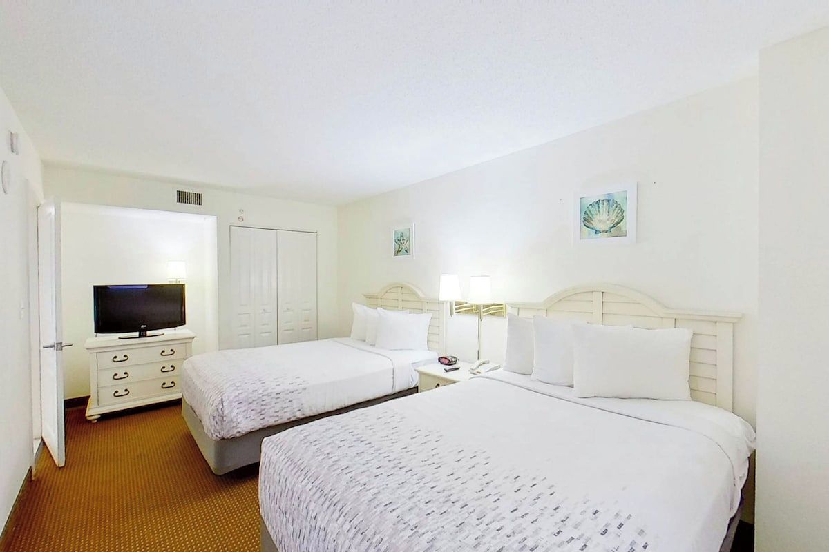 Een hotelkamer met twee bedden, een televisie, een kledingkast en een badkamers deur.
