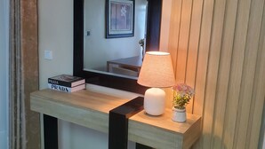 Une pièce comprenant une console en bois, un miroir, une lampe et un vase avec des fleurs.