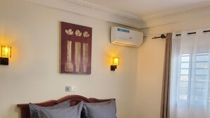 Une chambre à coucher avec un lit en bois, deux lampes fixées au mur, un luminaire au plafond et un appareil de climatisation.