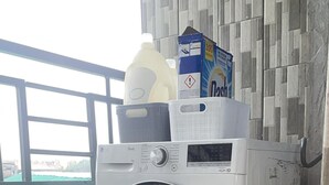 Un lave-linge à chargement frontal, doté d’un panneau de commande, d’un bidon de lessive et d’une boîte placée sur le dessus.