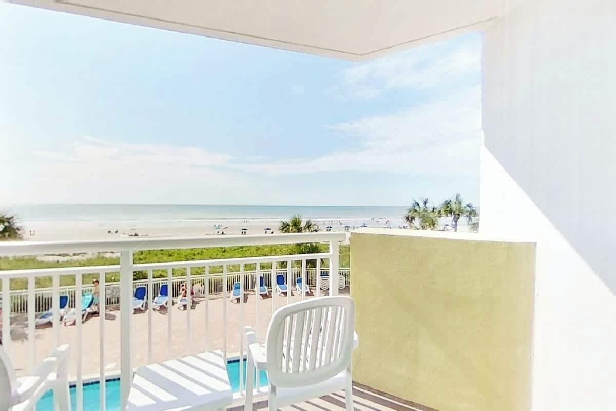 Un balcon avec vue sur la plage, une piscine et des chaises longues.