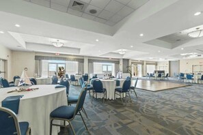 A spacious hotel conference room with round tables and blue chairs, large windows, and a carpeted floor. - Bay Watch Resort 0234 (North Myrtle Beach)