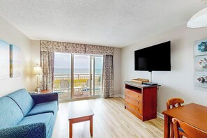 Ein Hotelzimmer mit einer Couch, einem Fernseher, einer Holzkommode und einem Balkon mit Blick.