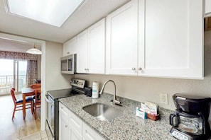 A compact kitchen with white cabinets, a granite countertop, a coffee maker, and a microwave. - Bay Watch Resort 0234 (North Myrtle Beach)