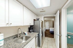 Eine Küche mit weißen Schränken, einer Granit Arbeitsplatte und Edelstahlgeräten. Im Hintergrund ist ein Badezimmer zu sehen.