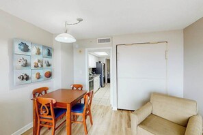 A dining area with a wooden table and chairs, a sofa, and a wall with decorative shells. - Bay Watch Resort 0234 (North Myrtle Beach)