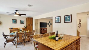 A spacious dining area with a large wooden table, surrounded by wicker chairs, and a television in the background. - Buttonwood Corner by Avantstay Midtown Key West Private Pool + Tropical Patio Near Beaches (Key West)