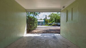 Vista a través d'una porta cap a una zona exterior coberta, amb un camí de grava que condueix a un edifici amb teulada blava.