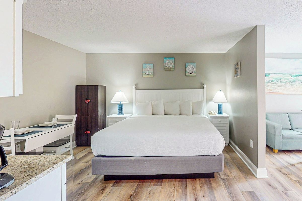 A bedroom with a large bed, bedside tables, a desk, and a view of the ocean.