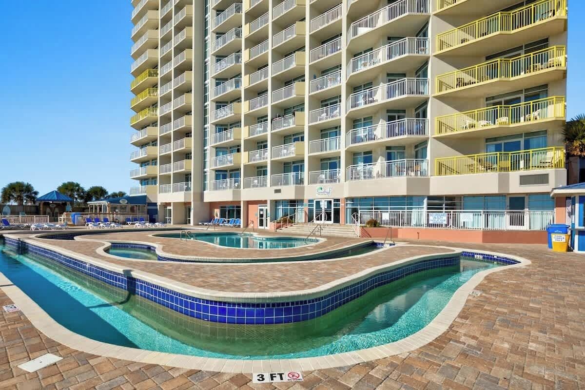 Ein mehrstöckiges Hotel mit Poolbereich, der ein gewelltes Design und eine maximale Tiefe von 90 Zentimetern aufweist.