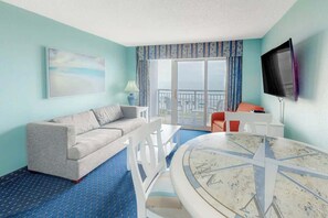 Ein Hotelzimmer mit Sofa, Esstisch, Fernseher und einem Balkon mit Blick.